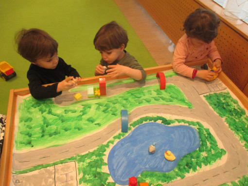 Kinder konstruieren mit Bausteinen auf einer selbst gemalten Landschaft