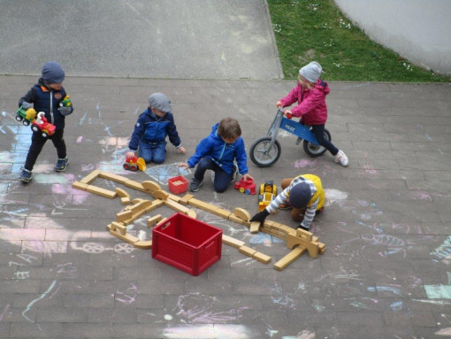 Kinder legen im Garten eine große Figur aus Holz und malen mit Straßenkreide
