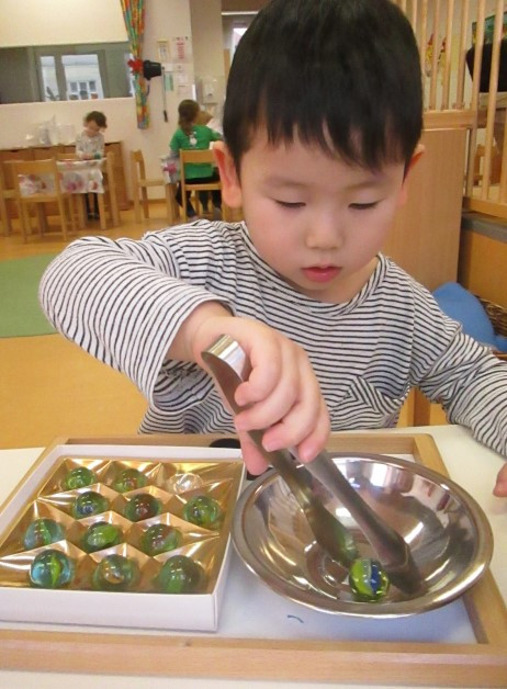Ein Junge legt konzentriert Glaskuglen, mit einer Greifzange, von einer Schüssel in eine Schachtel 