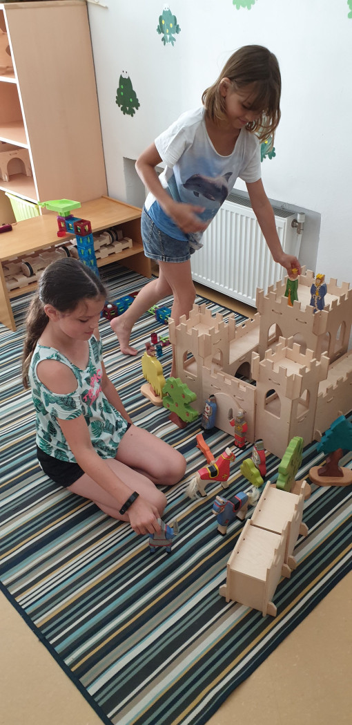 Zwei Mädchen gestalten gemeinsam eine Geschichte mit einer Holzburg und passenden Holzfiguren 