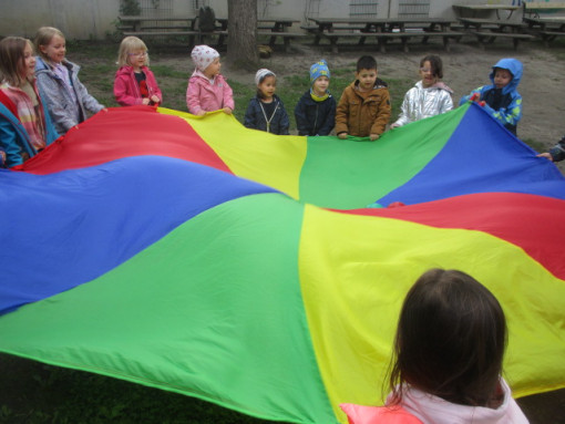 Kinder halten gemeinsam ein großes buntes Tuch im Garten