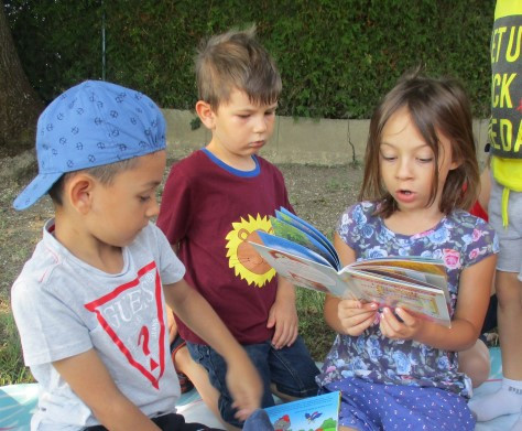 Mädchen liest zwei Buben aus einem Buch vor 