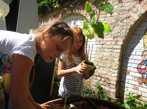 Zwei Mädchen Topfen behutsam eine Pflanze ein im Garten