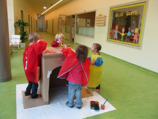 Vier Kinder bemalen gemeinsam ein Kartonhaus