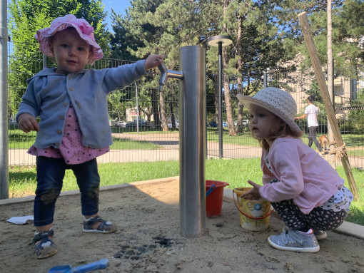 Kinder am Wasserhahn im Garten bei der Sandkiste