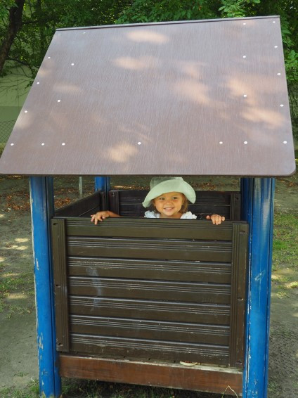 Ein Mädchen versteckt sich verschmitzt, in einer Holzhütte, im Garten 
