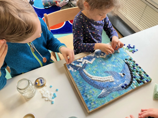 Zwei Kinder gestalten einen Delfin mit Mosaiksteinen