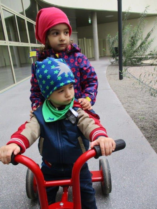 Zwei kinder fahren auf einem Dreirad durch den Garten 