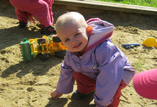 Ein kleines Kind spielt lächelnd in der Sandkiste