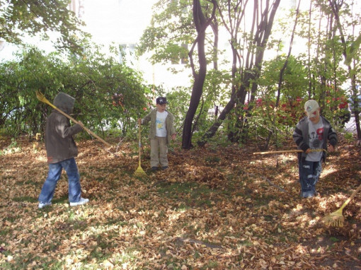 Drei Kinder rächen spielerisch Herbstlaub im Garten