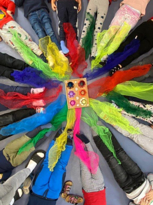 Kinder stellen den Wert Vielfalt liegend im Kreis um eine Farbpalette und Farbtüchern