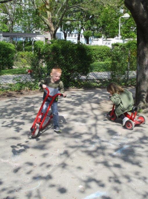 Zwei Kinder düsen mit Tretfahrzeugen durch den Garten