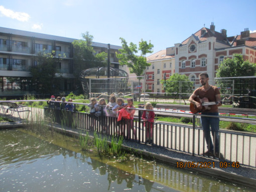 Kinder betrachten gemeinsam einen Teich und hören einem Gitaristen zu