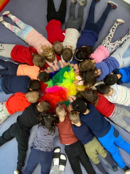 Kinder stellen den Wert Vielfalt im Kreis um Farbtücher liegend dar