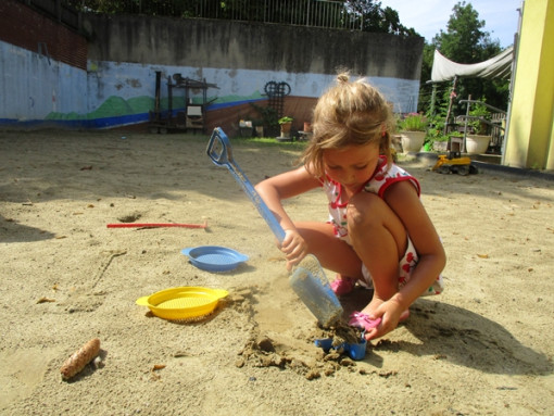 Ein Mädchen, in der Sandkiste, schaufelt konzentriert Sand in eine blaue Form