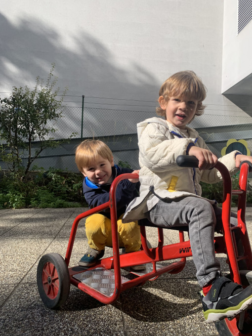 Zwei Kinder fahren mit einem Tretfahrrad im Garten