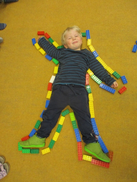 Ein Junge liegt glücklich auf einem Teppich, umrahmt von Duplosteinen