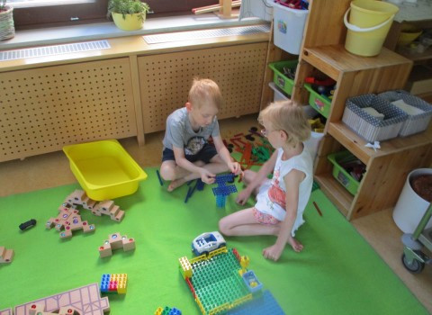 Zwei Kinder bauen gemeinsam ein Gebäude aus Duplosteinen