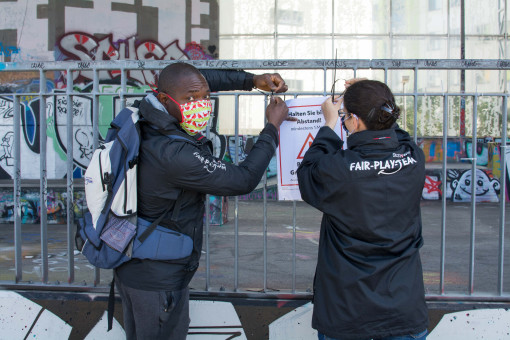 Zwei Mitarbeiter*innen der Fair-Play-Teams hängen Plakate auf