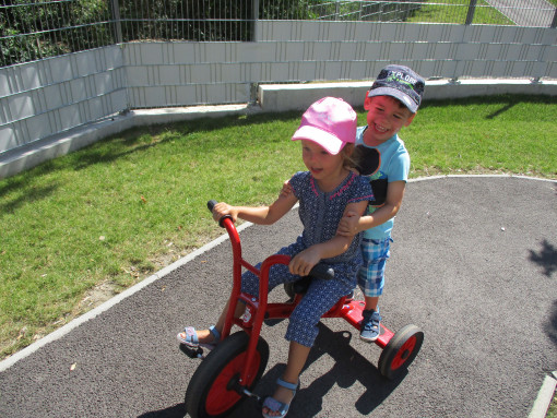 2 Kinder fahren auf einem Dreirad im Garten