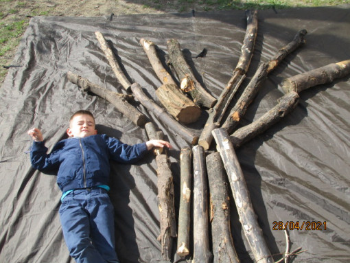 En Kind liegt neben Holzbaustämmen im Garten
