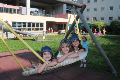 Kinder liegen strahlend auf der Korbschauschaukel im weitläufigen Garten