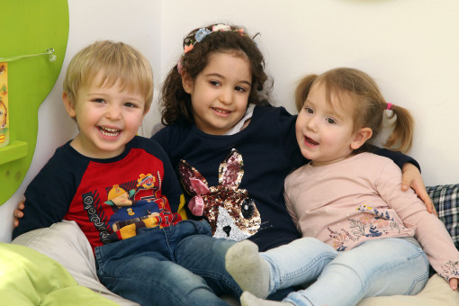 Kinder sitzen zu dritt zusammen, umarmen sich und lachen