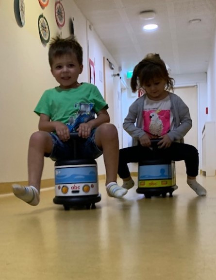 Zwei Kinder fahren auf Spielzeugbussen durch den Gang