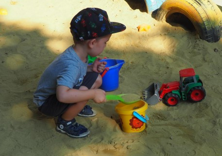 Ein Junge schaufelt, in der Sandkiste, Sand in einen Kübel